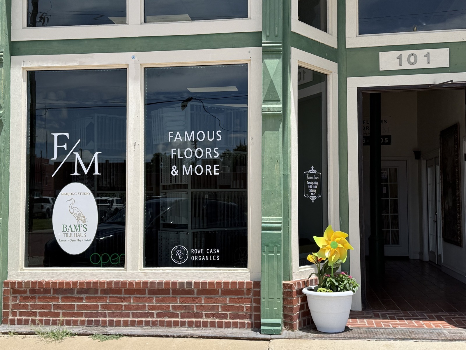 Green and white storefront of Famous Floors and More, with Bam’s Tile Haus heron sign in the window and the entrance marked 101